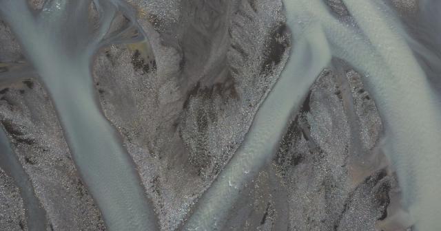 A winding glacial river traces blue and grey patterns across dark terrain.