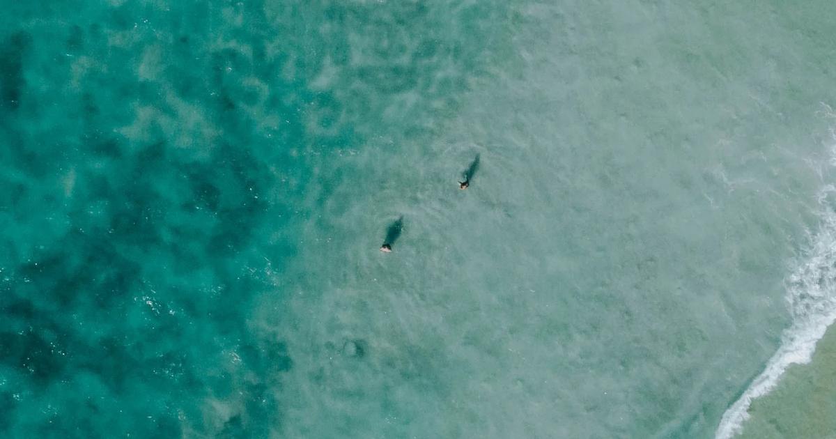 Pale waves roll across turquoise water toward a sandy beach.