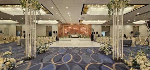 Ballroom set for a reception: crystal-strand pillars topped with florals frame a white dance floor leading to a champagne drape stage, with ivory chairs on either side.