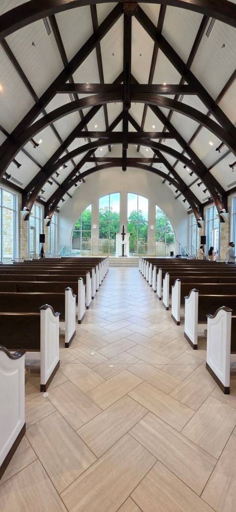 Chapel with dark timber trusses and white pews, the aisle leading to a ceremony setting beneath tall arched windows.
