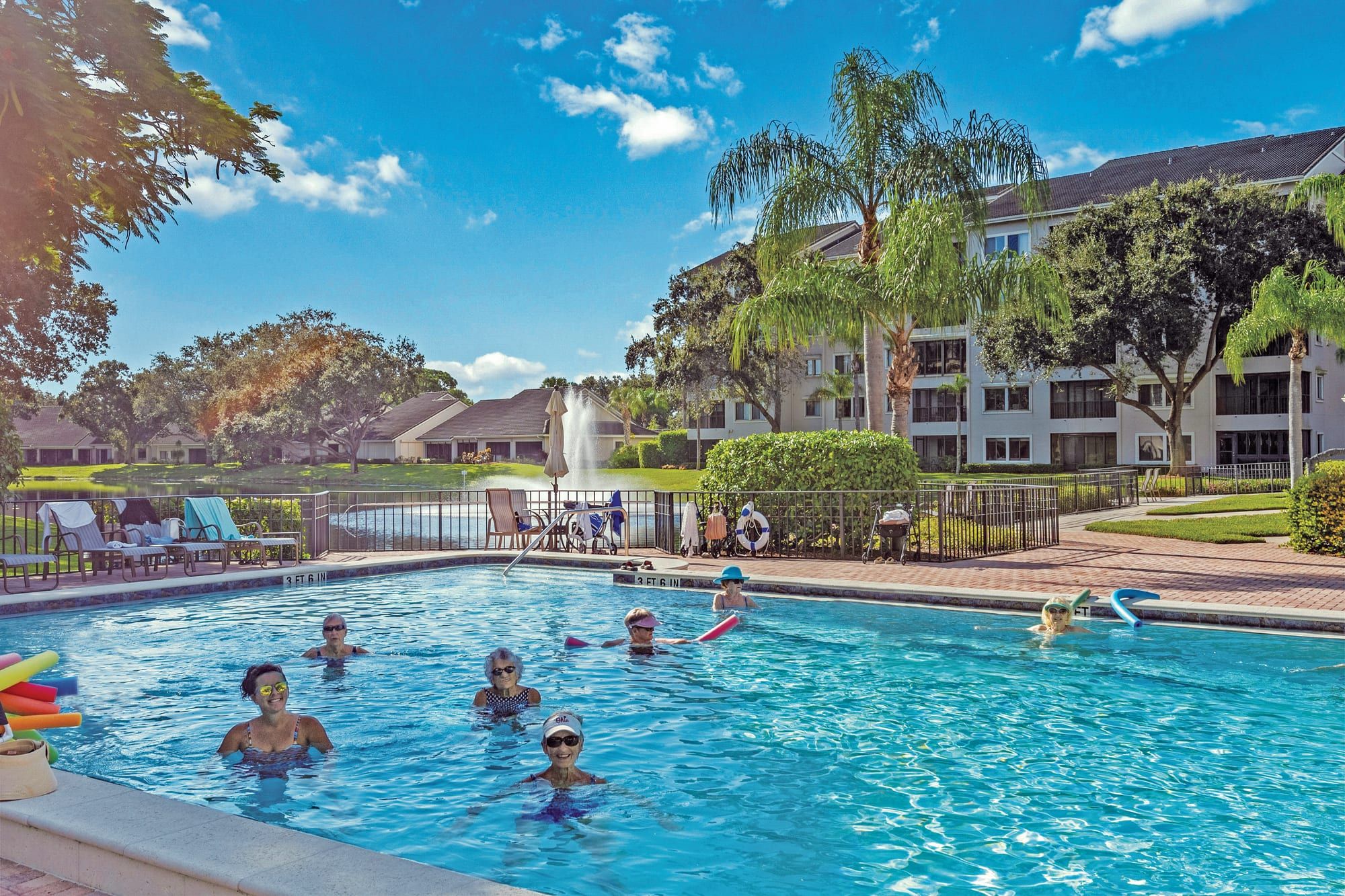 Residents swimming in the heated pool beside the clubhouse, under palms and a blue sky