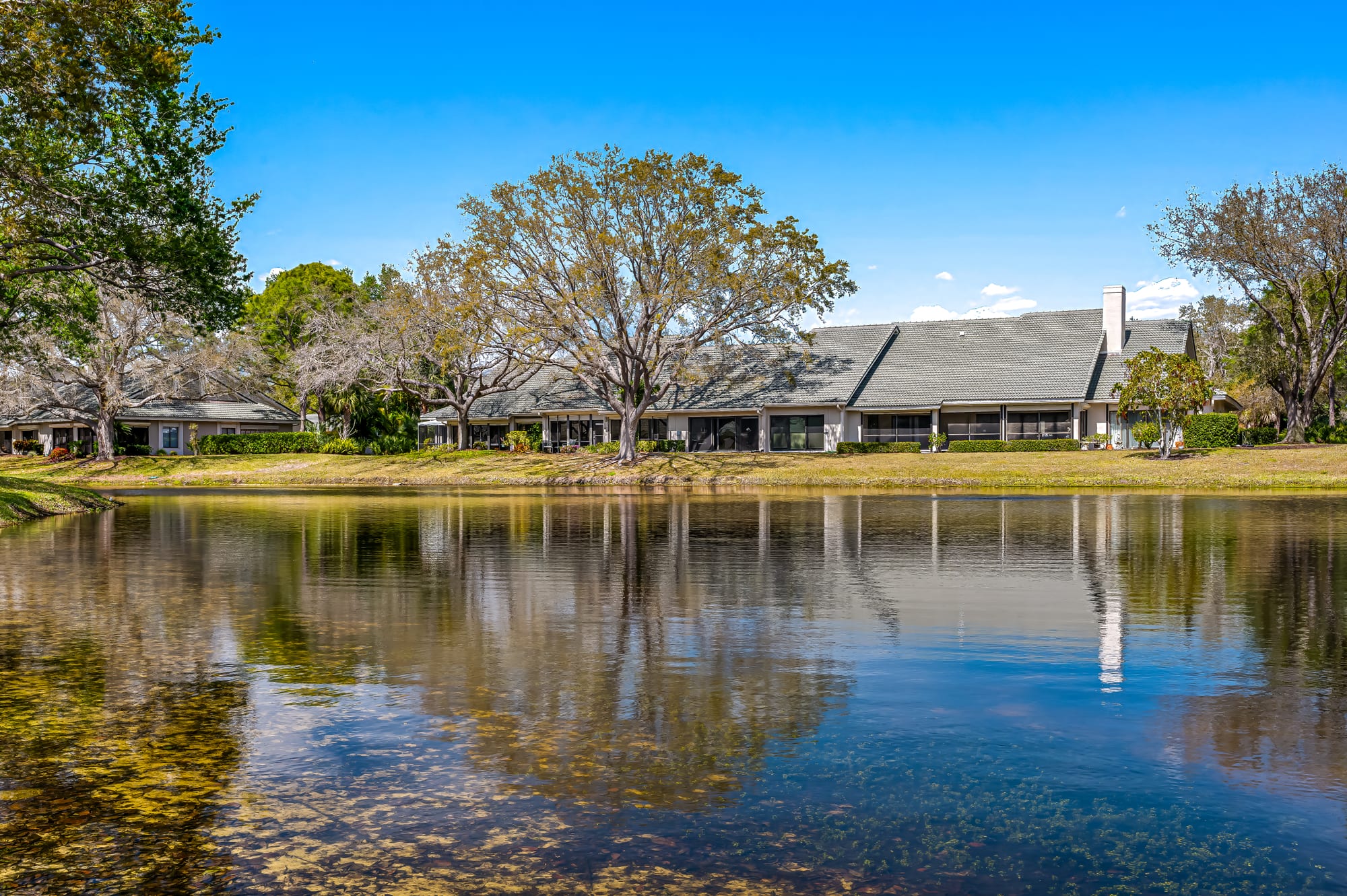 Single-story villas among the oaks, reflected in Arbor Lake