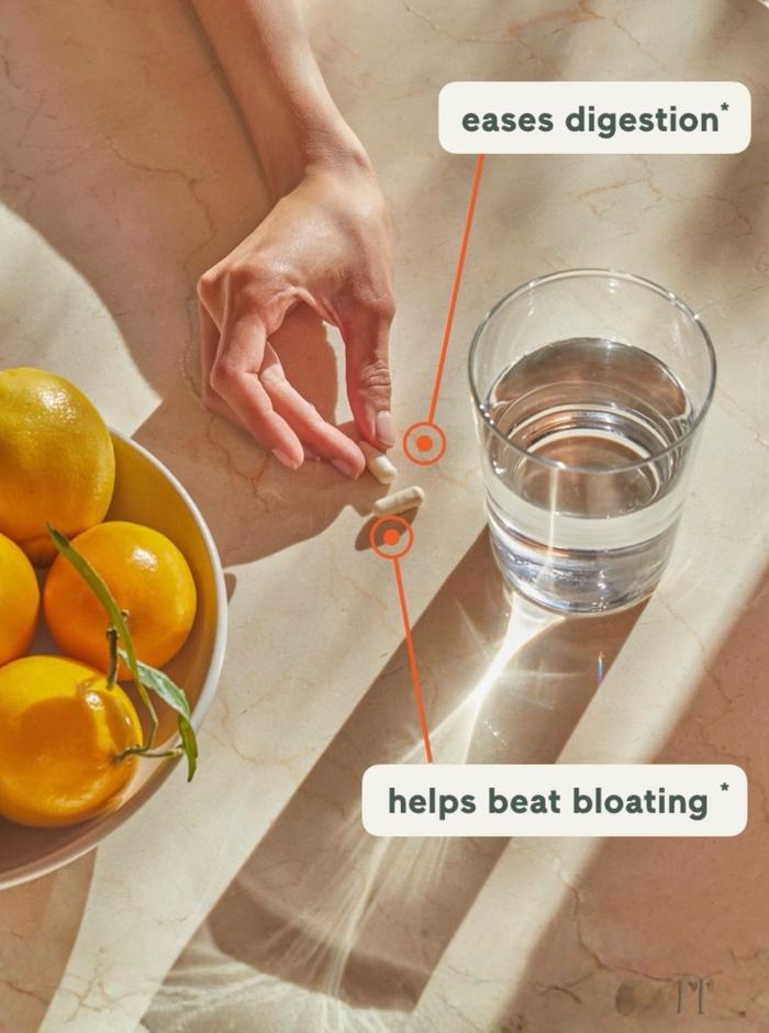 Overhead shot of a hand picking up a probiotic supplement on a table with a glass of water with light streaming in on the table.