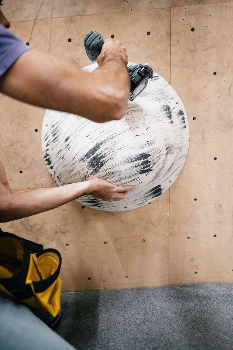 Matthias Woitzuck mounting a climbing volume to the wall with a screwdriver.