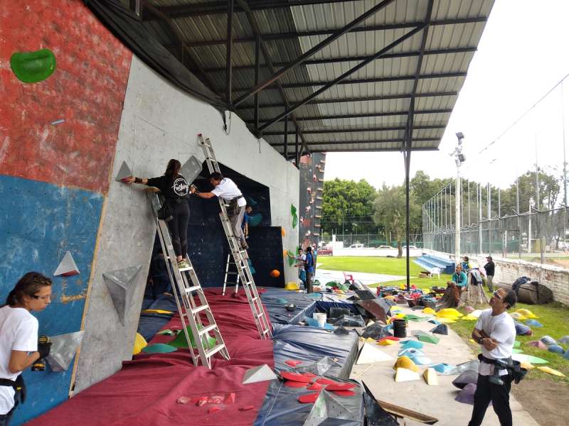 A team of routesetters working on a bouldering wall under a roof.