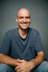 Matthias Woitzuck laughing in front of a climbing wall, hands resting on his thighs.