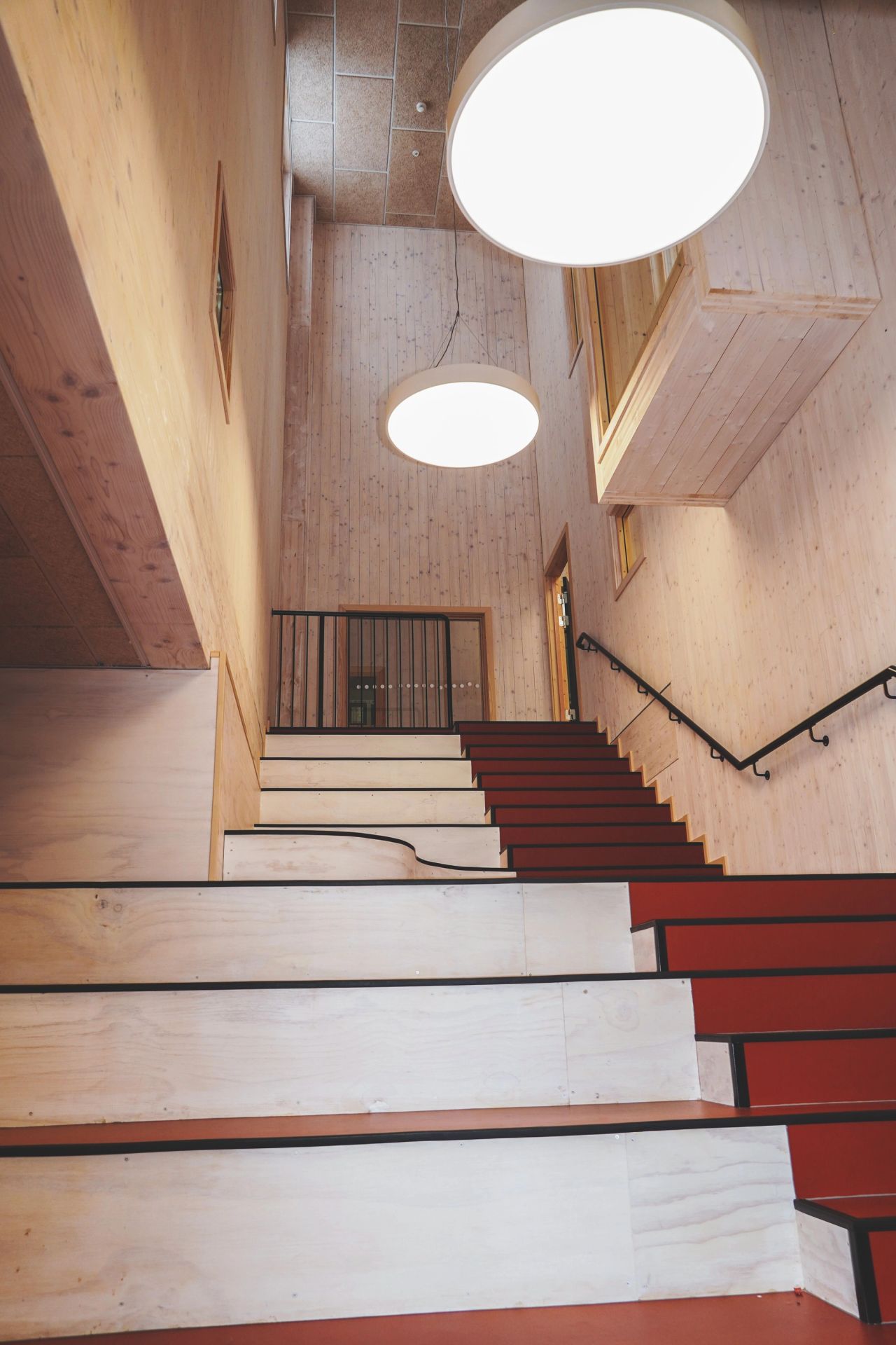 Trappeområde på Ydalir skole med trevegger, røde trinn og store runde taklamper.