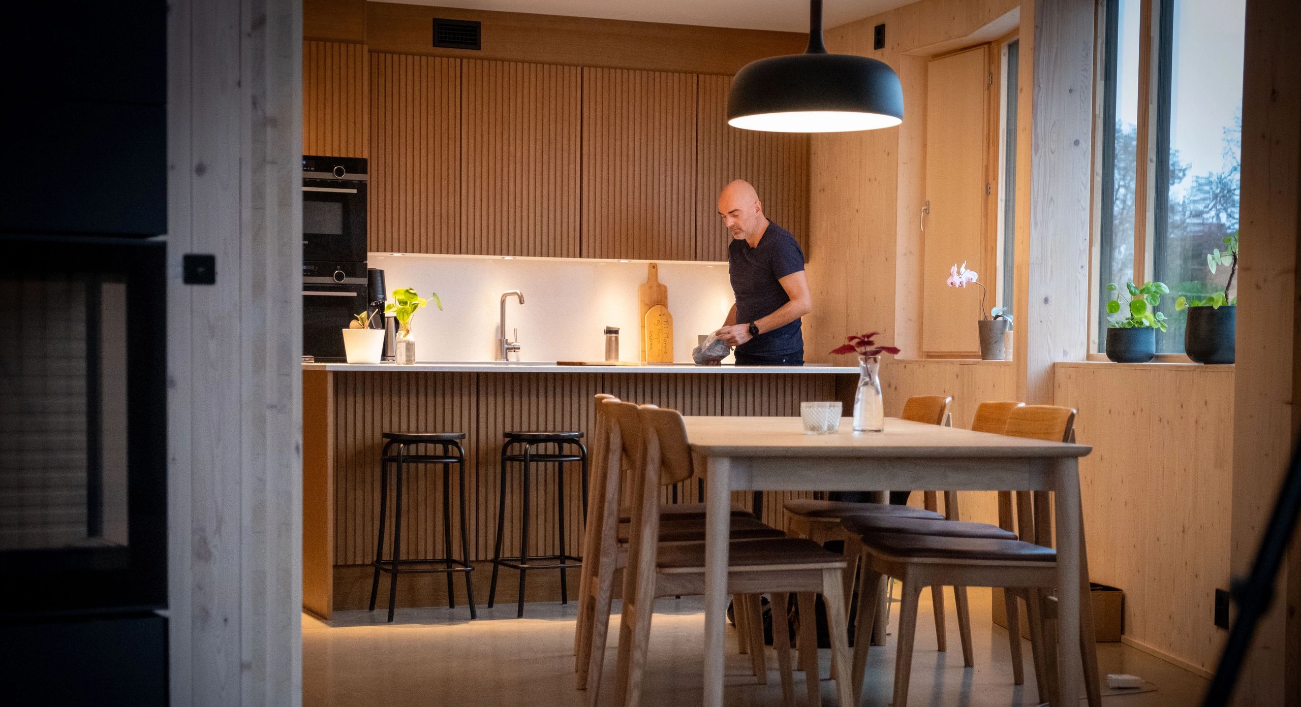 Nikolaos Farmakis står på kjøkkenet i boligen sin, omgitt av treflater og store vinduer