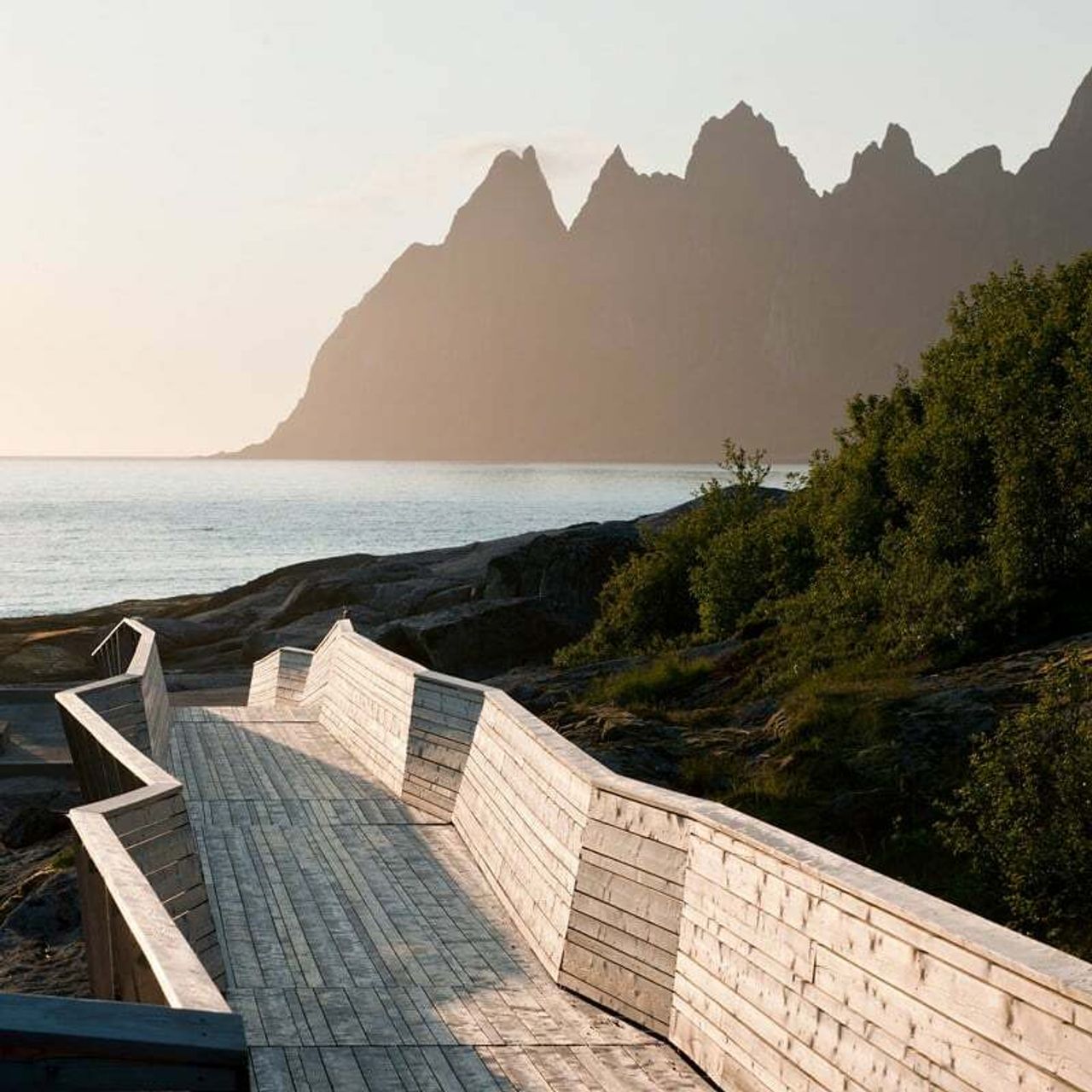 Trebygd gangsti med gelender langs kysten på Senja, med fjell og hav i bakgrunnen.