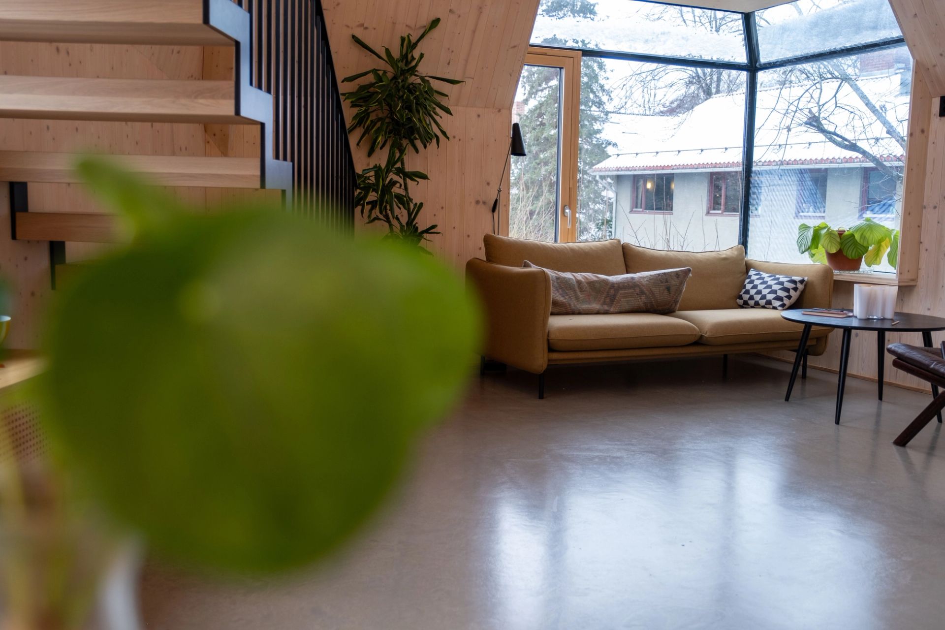 Stue med synlige treflater, stor hjørnevindusflate, sofa og trapp i leiligheten i Geitmyrsveien 36