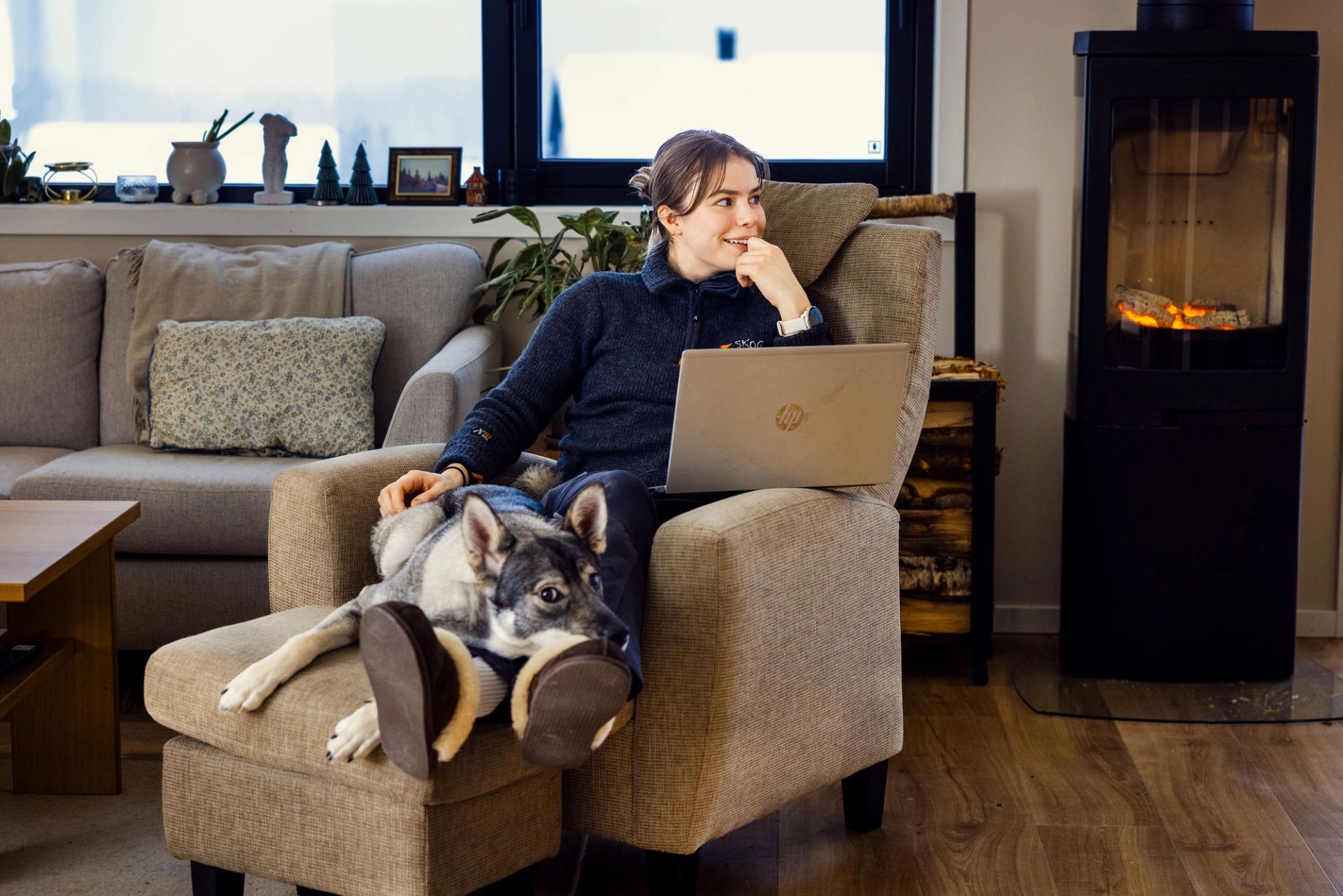 Viil Flaata sitter hjemme med bærbar PC i fanget og hunden ved føttene foran en vedovn.