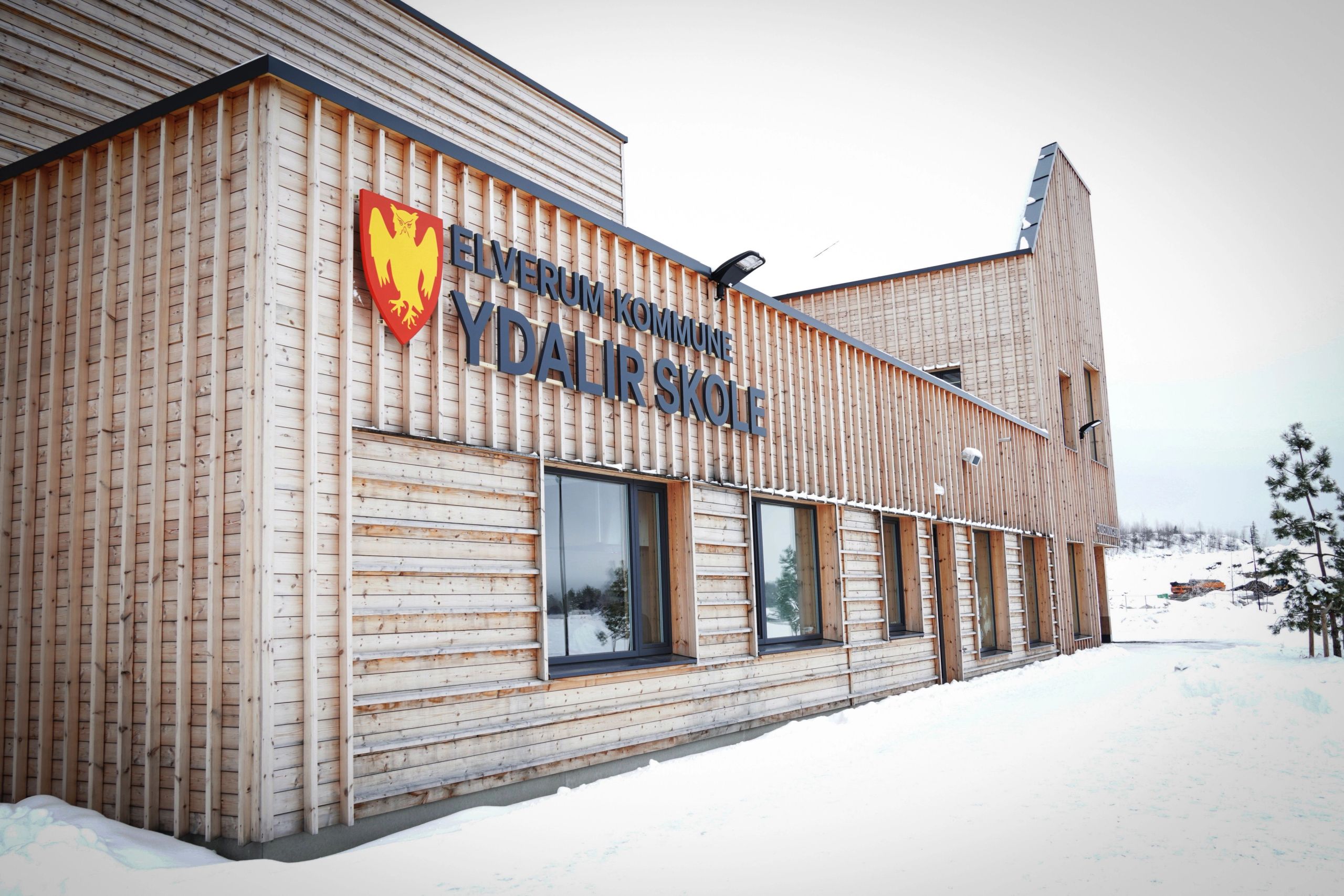 Ydalir skole i Elverum med fasade i tre og skolens navn på veggen, omgitt av snø.