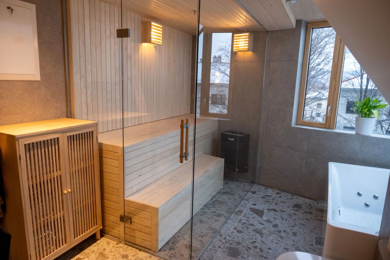 Bad med badstue i tre, glassvegg og vinduer mot nabolag.