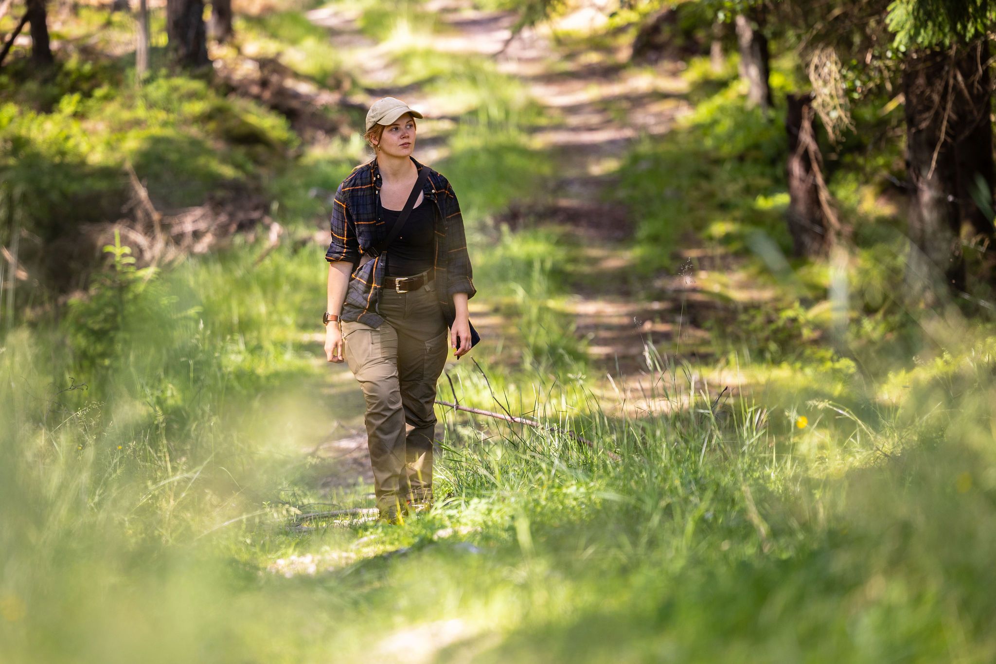 Elin Johanne går gjennom skogen på en solfylt skogsvei.
