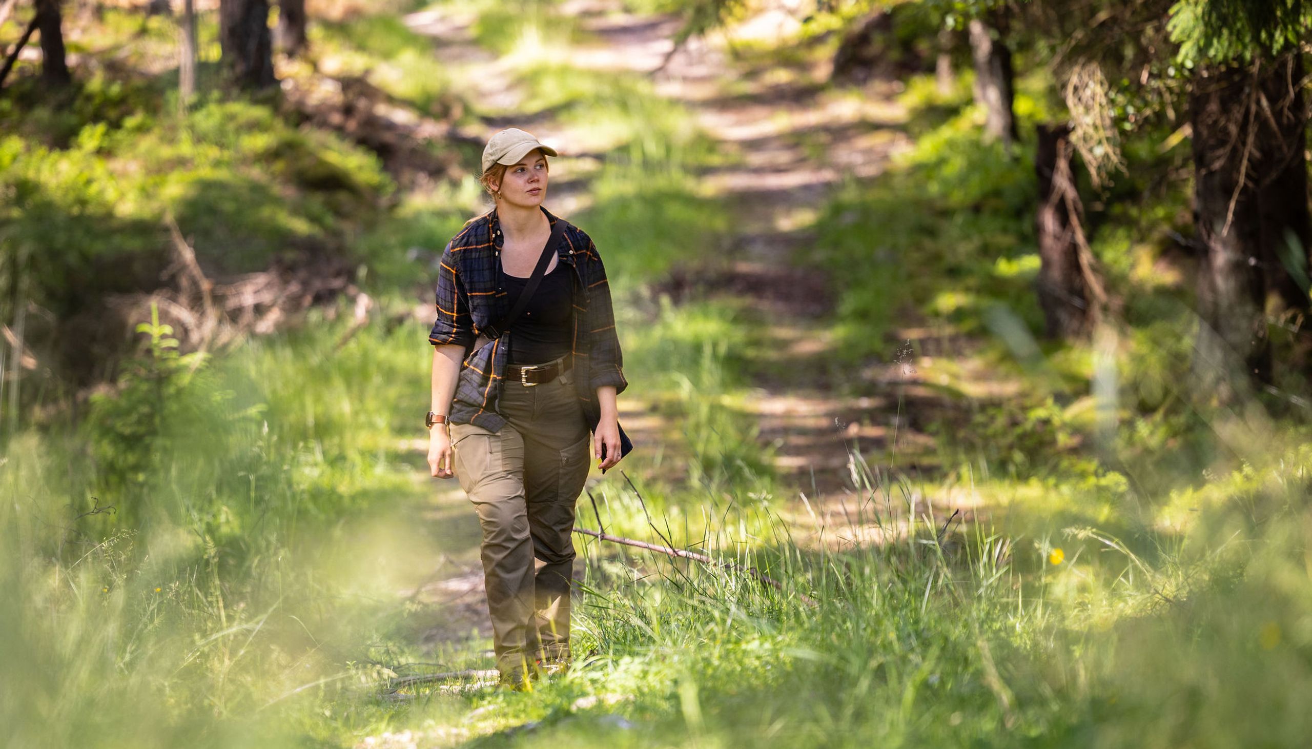 Elin Johanne går gjennom skogen på en solfylt skogsvei.