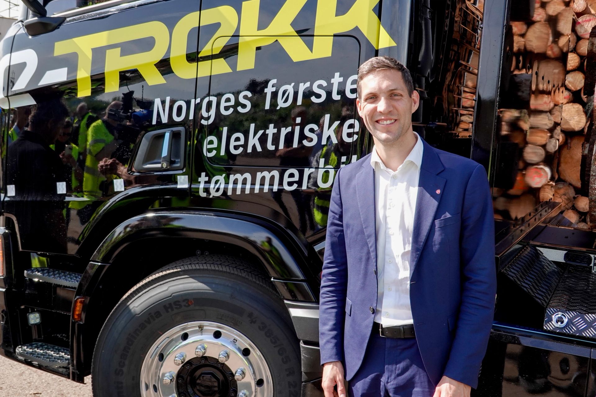 Klima- og miljøminister Andreas Bjelland Eriksen smiler foran Norges første elektriske tømmerbil