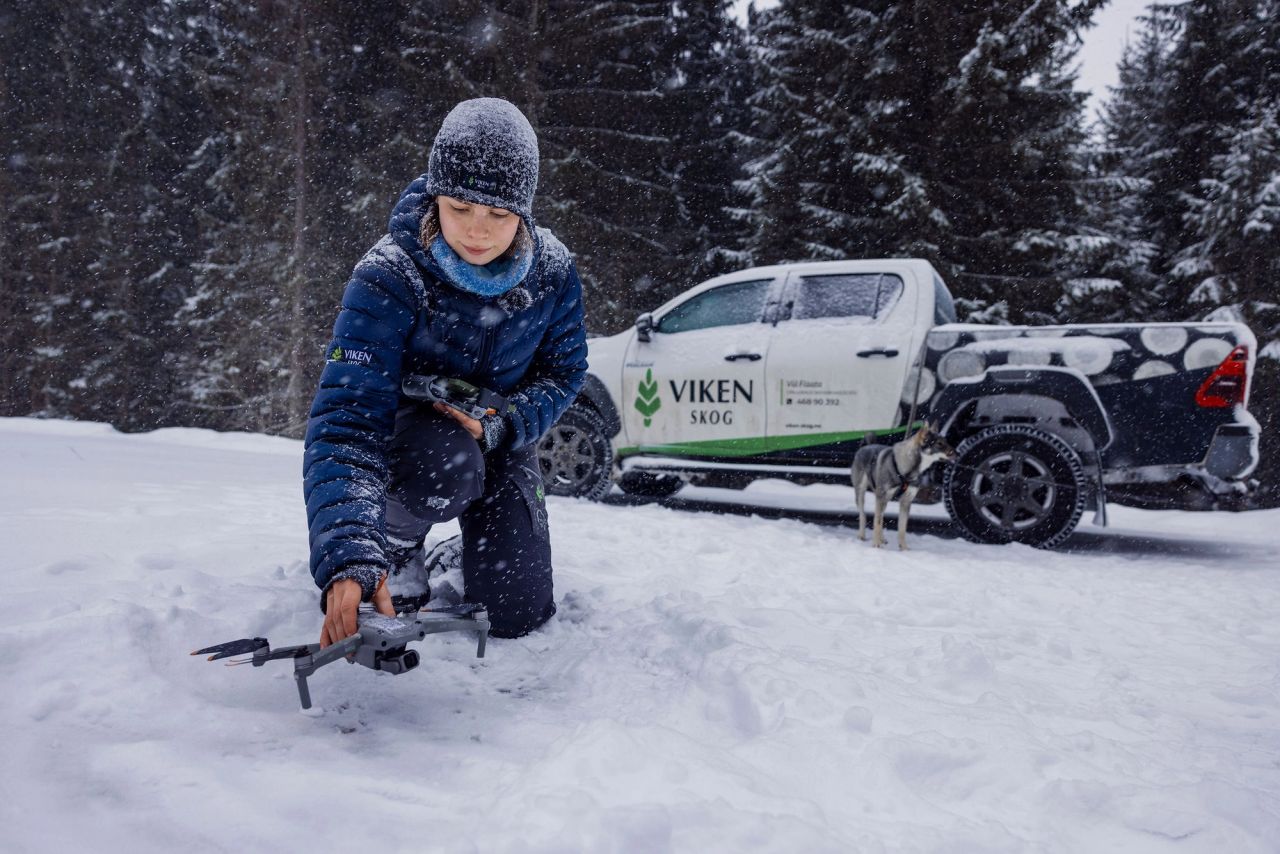 Viil Flaata gjør klar en drone i snøen ved en bil fra Viken Skog.