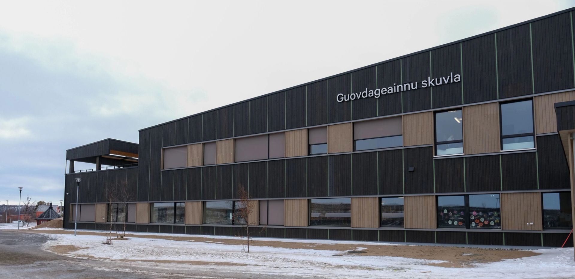 Fasaden på Guovdageainnu skuvla, Kautokeino skole, med mørk trekledning og lyse trefelt.