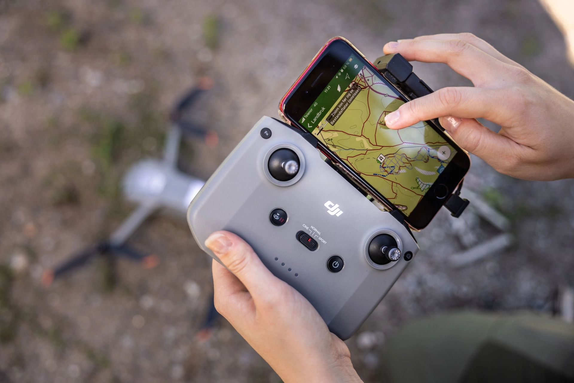 Nærbilde av hender som bruker dronekontroll med kart på mobilskjermen.