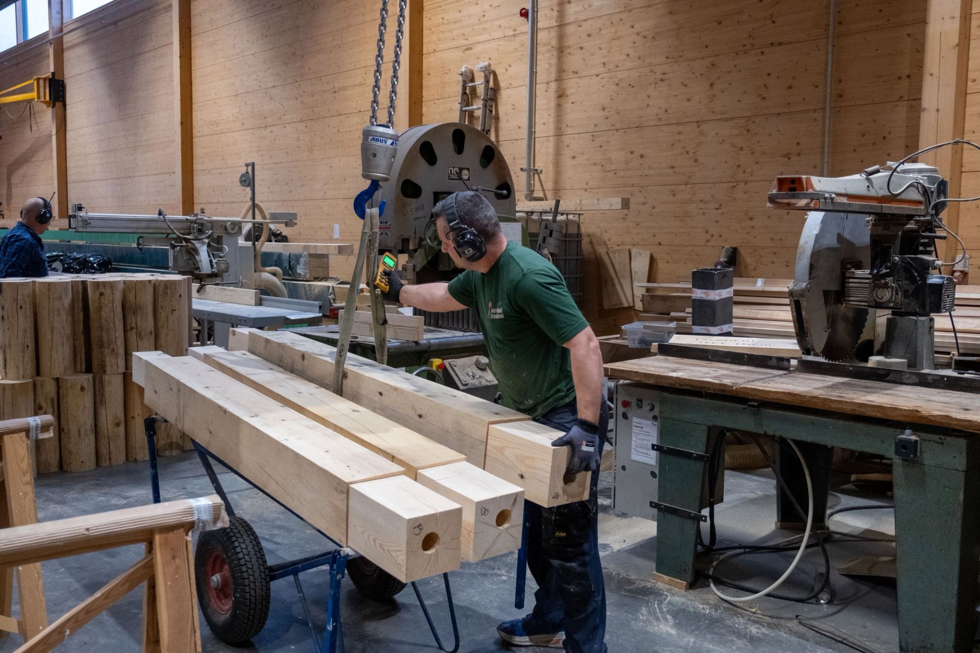 Ansatt arbeider med store treemner og maskiner i produksjonshallen hos Aanesland Treindustri.