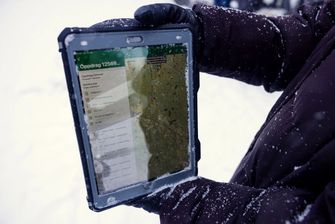 Nærbilde av nettbrett med digitalt skogkart og oppdragsinformasjon ute i snøvær.