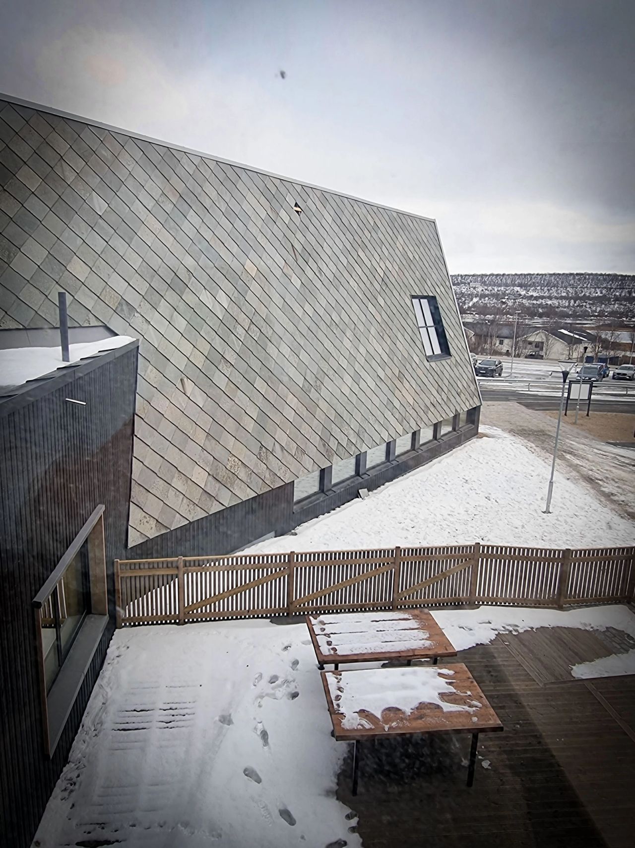 Utsiden av skolen med store flater kledd i grå Altaskifer og snø på bakken.