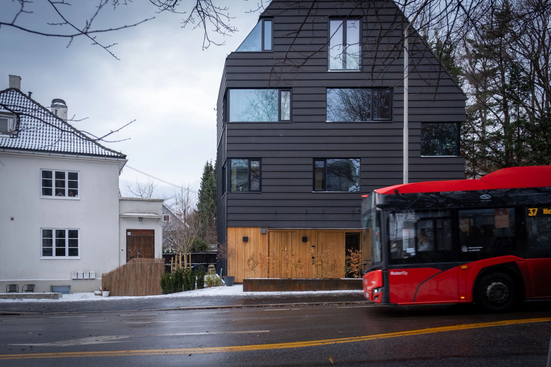 Det mørkkledde leilighetsbygget i Geitmyrsveien 36, med en rød buss som passerer foran.