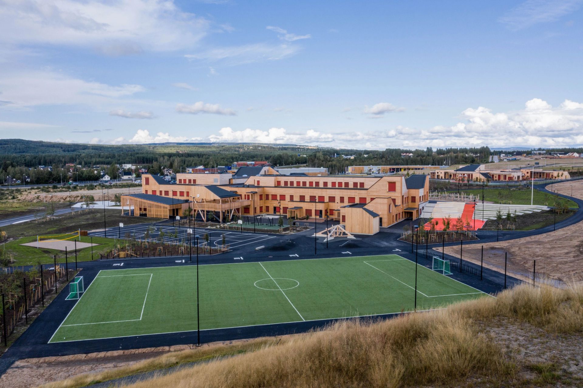 Oversiktsbilde av Ydalir skole i Elverum, et stort skolebygg i tre med fotballbane og uteområder foran.