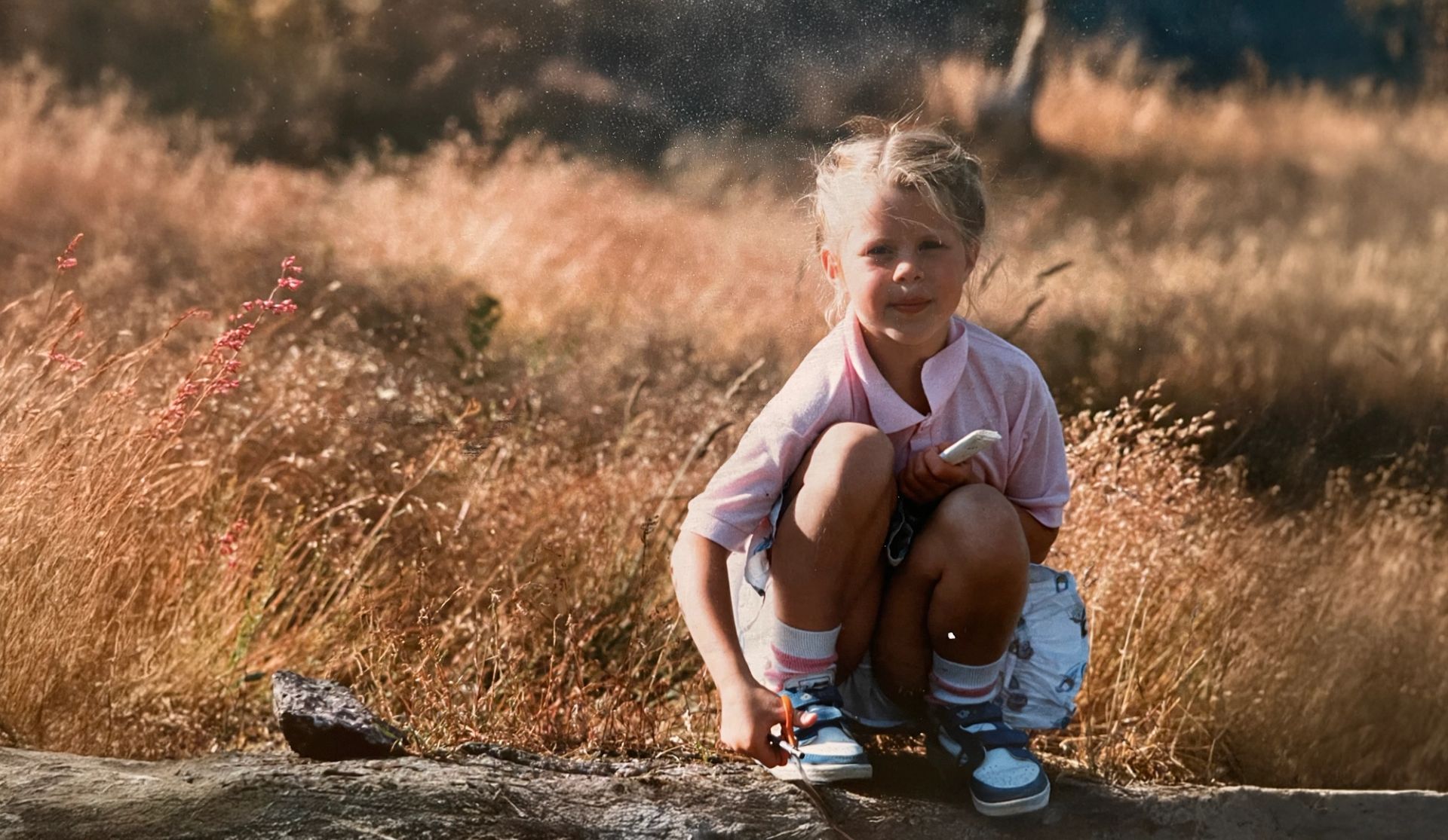 Barndomsbilde av Ane Christensen Tange sittende ute i lyng og gress.