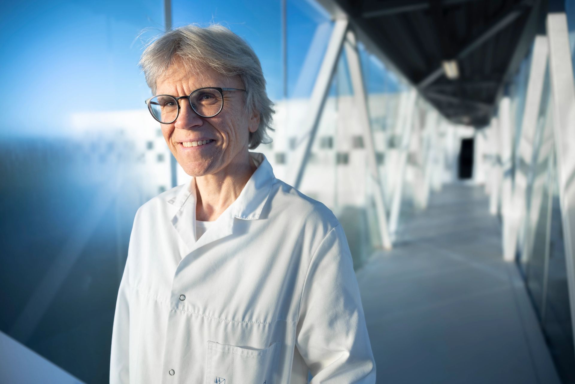 Kristin Misund med hvit laboratoriefrakk og briller står i en glasskorridor hos Borregaard.