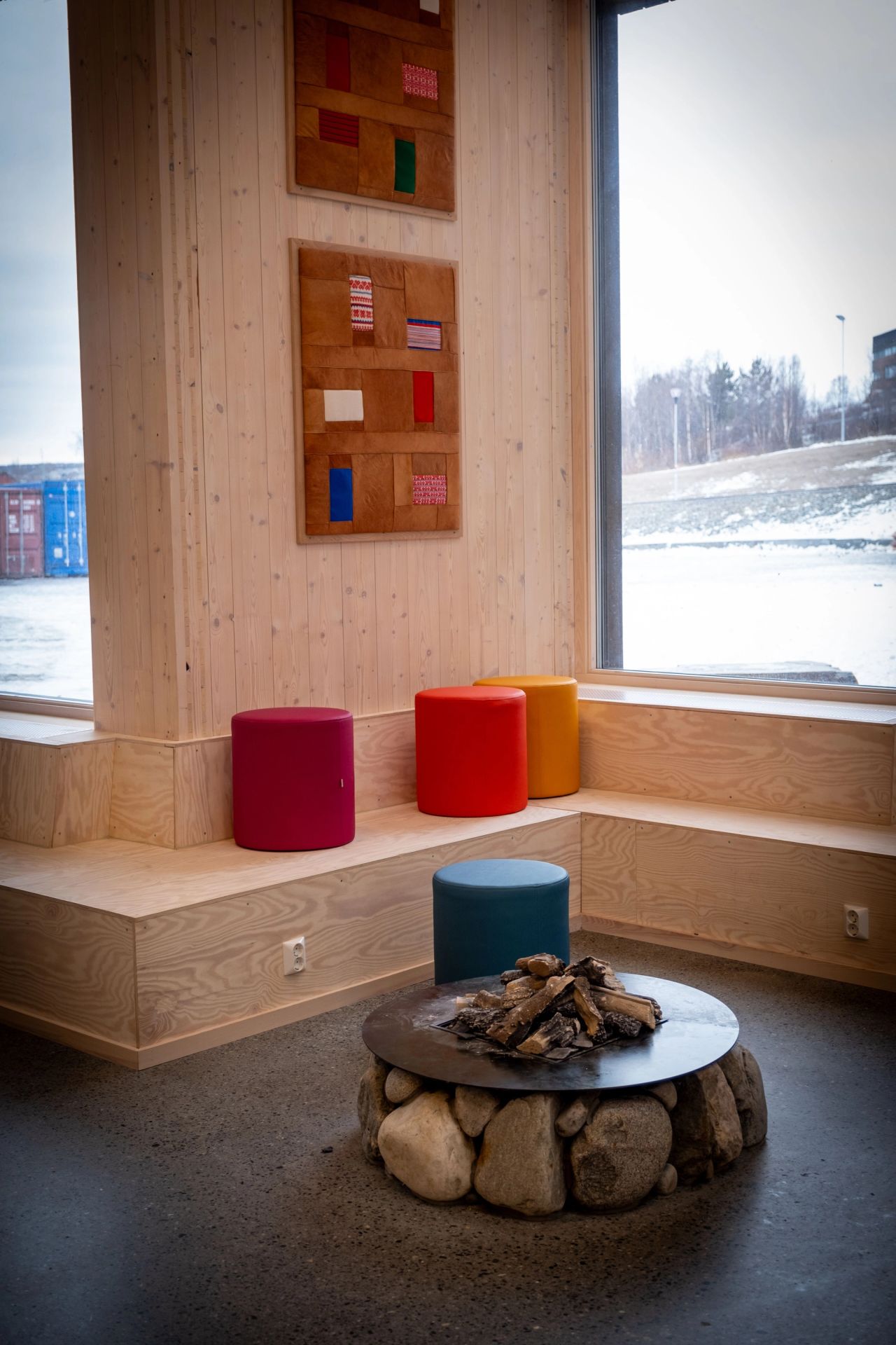 Sittekrok med ildsted, fargerike krakker og samisk kunst på veggen i skolens hjerterom.