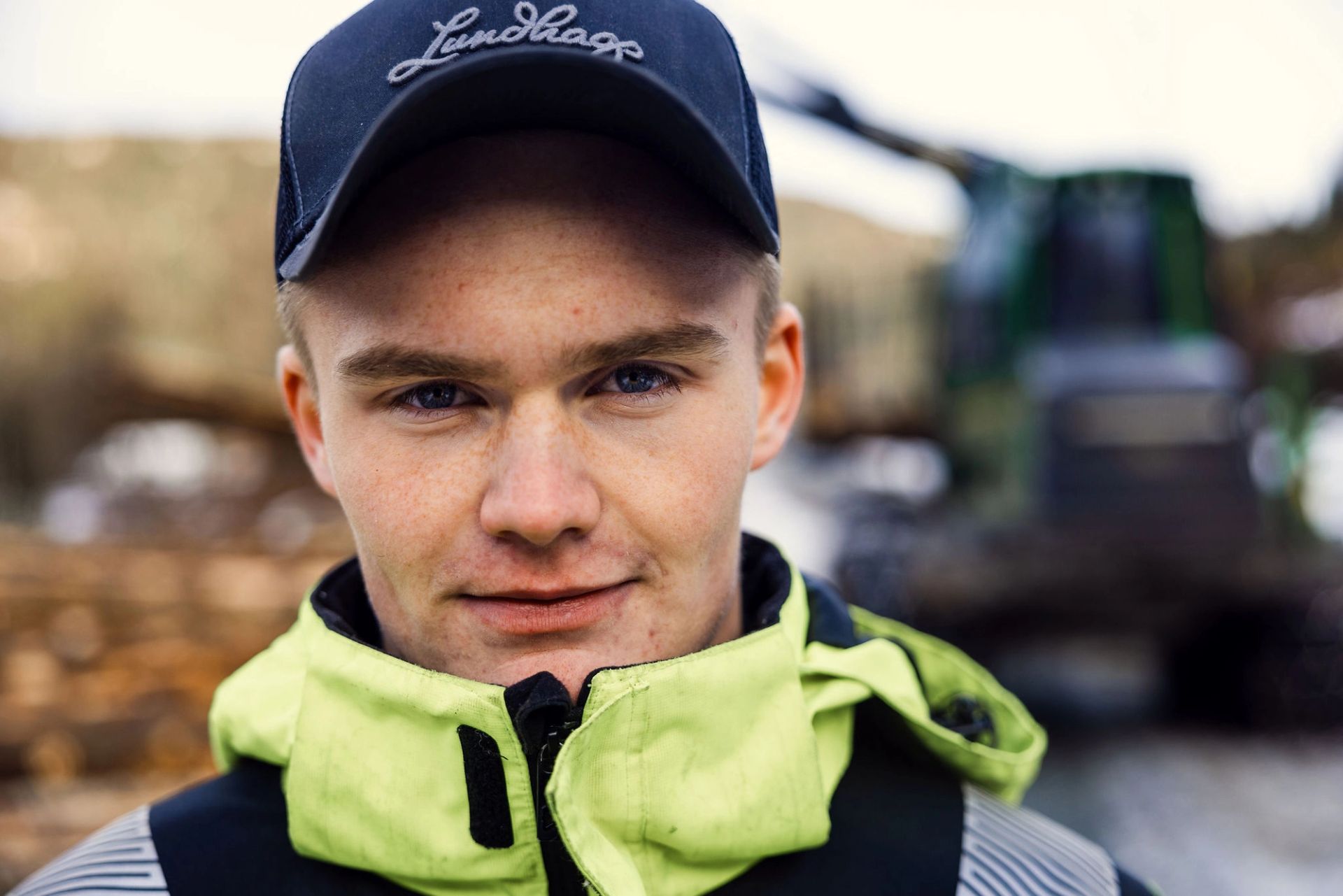 Nærbilde av Martin Næsbø med refleksjakke og caps, med skogsmaskin i bakgrunnen.