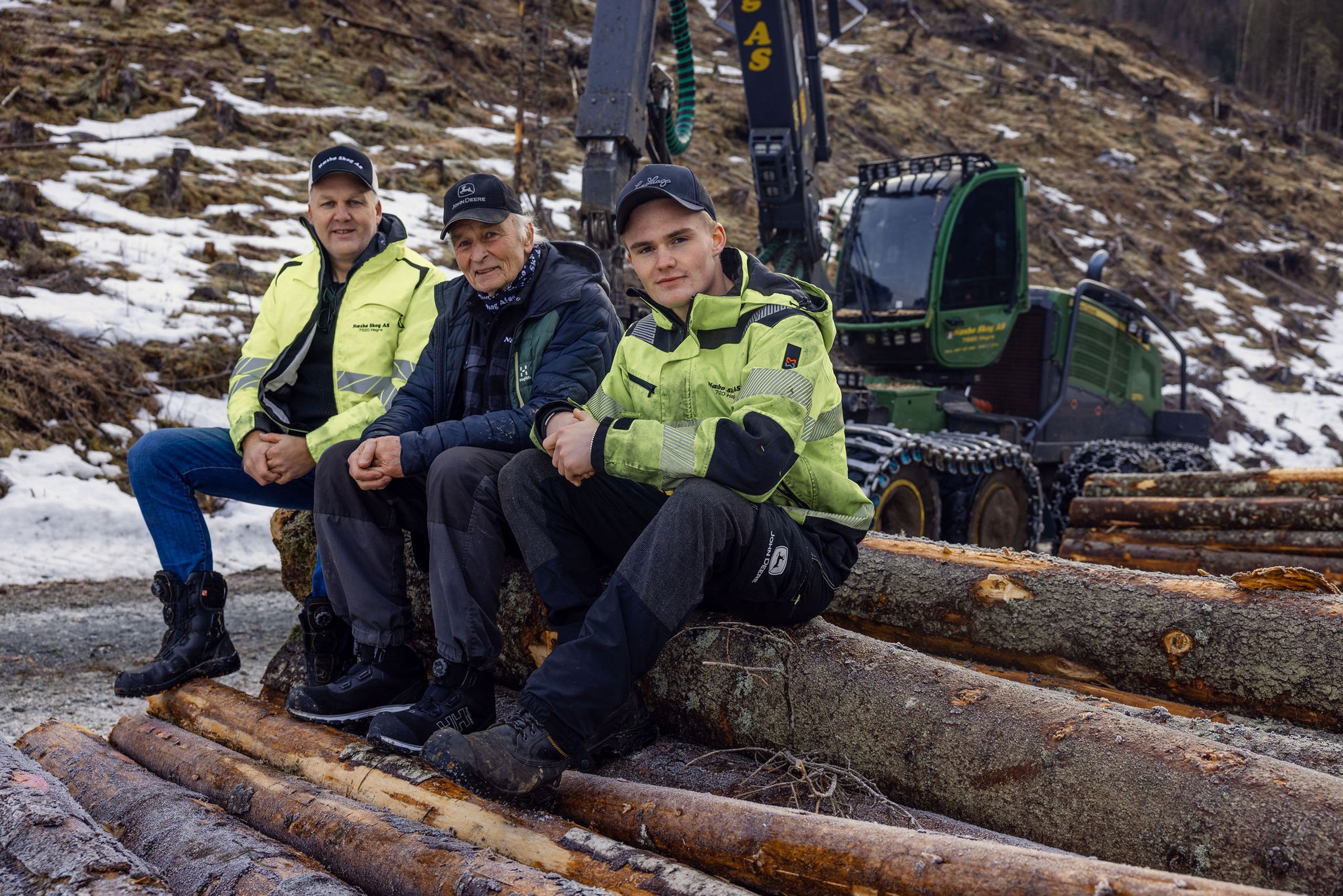 Torkil Næsbø, Leif Arnfinn Næsbø og Martin Næsbø sitter på tømmerstokker foran en skogsmaskin.
