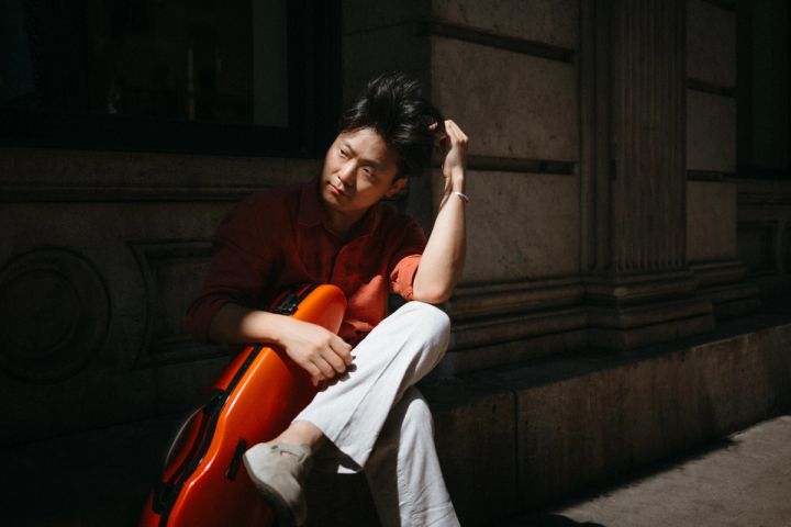 Siwoo Kim seated in warm shade with his red violin case