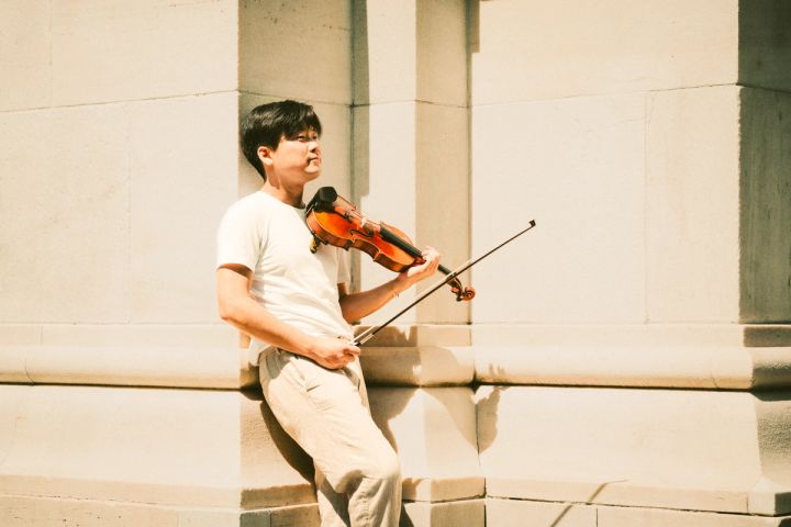 Siwoo Kim playing the violin against a stone wall