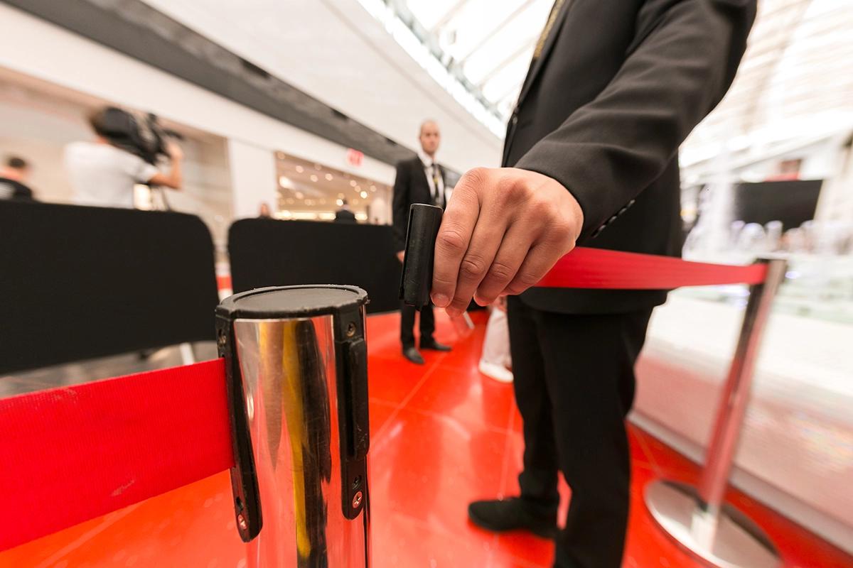 Security guard in a suit holding a red velvet rope at a club entrance, symbolizing strict door policy and club selection in Warsaw.