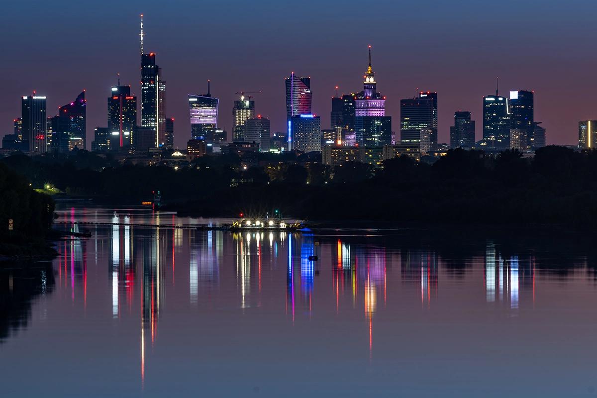 Night skyline of Warsaw with illuminated skyscrapers and the Palace of Culture and Science reflecting in the Vistula River