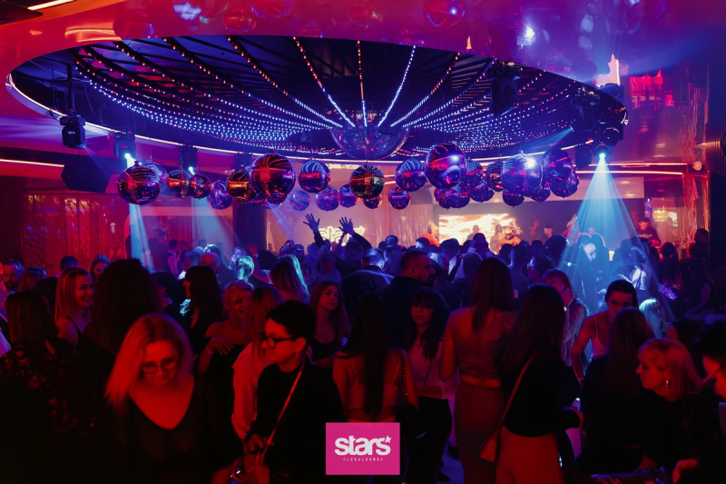 A wide view of the energetic dance floor at Stars Club & Lounge in Toruń, featuring dozens of silver disco balls suspended from a modern LED-lit ceiling in blue and purple hues.