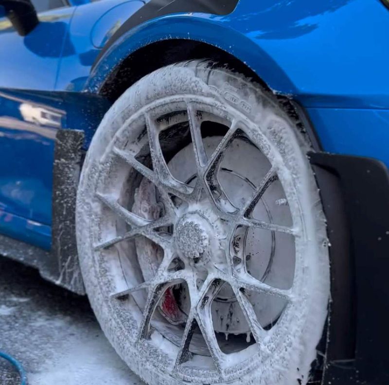 Snow foam on the wheel of a blue sports car