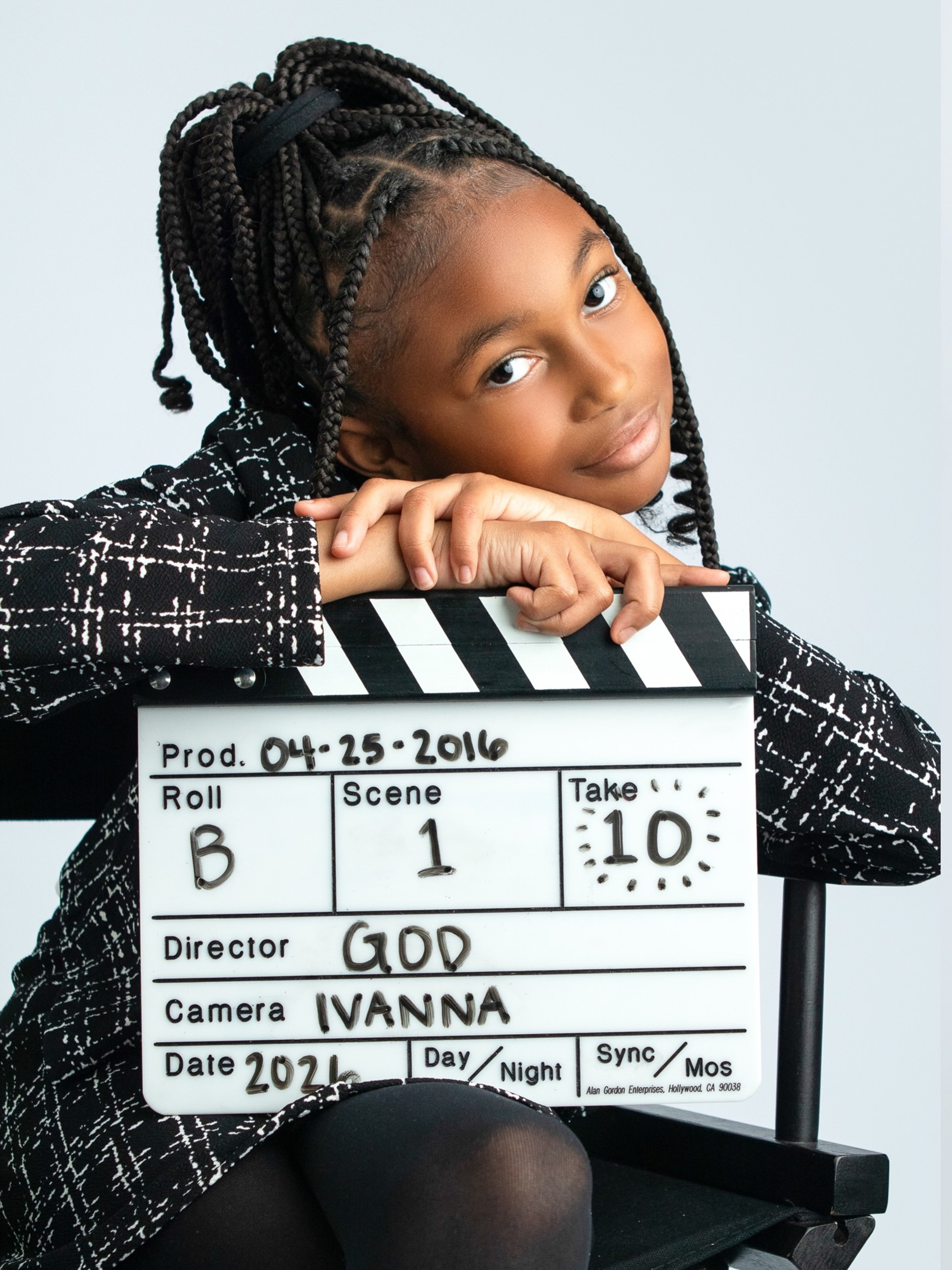 a Captured by J. Moïse milestone portrait — a young girl in a tweed blazer leaning on a film-set clapperboard