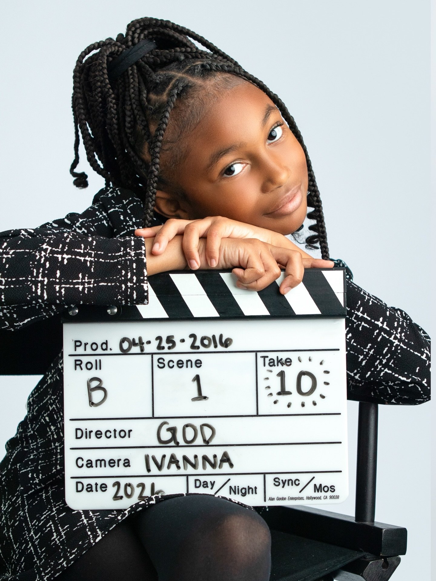 a Captured by J. Moïse milestone portrait — a young girl in a tweed blazer leaning on a film-set clapperboard