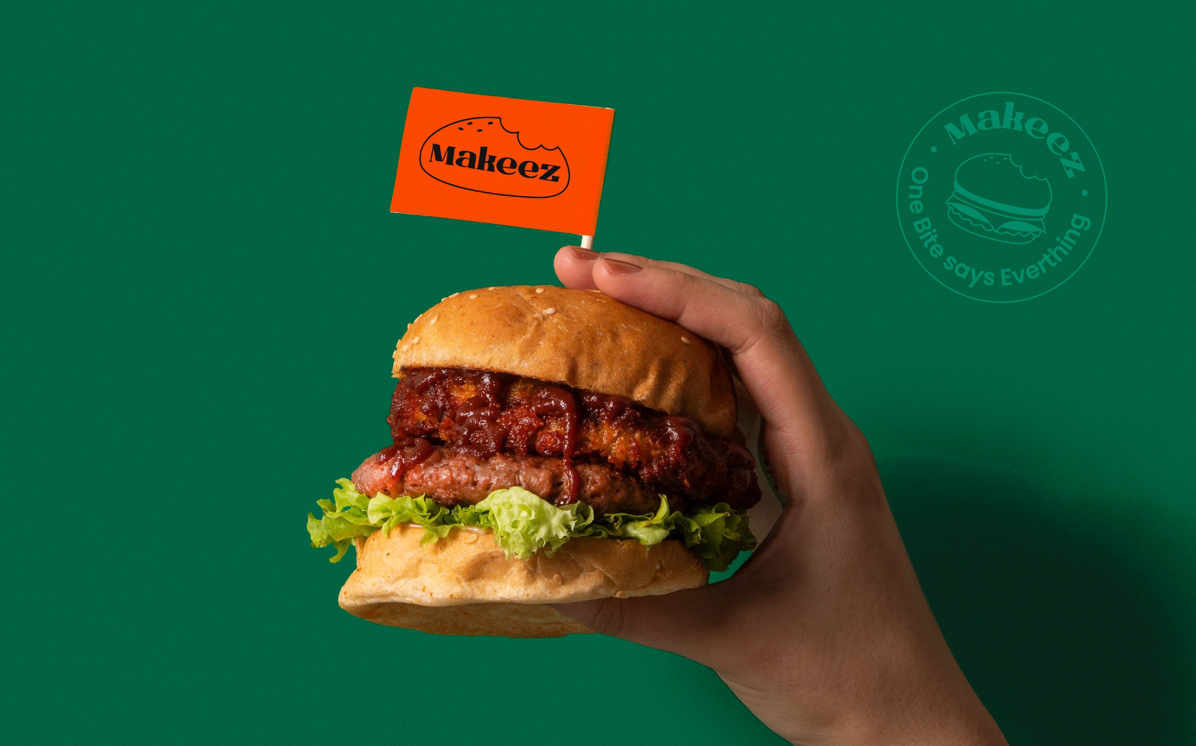 Hand holding a Makeez burger with a branded flag pick