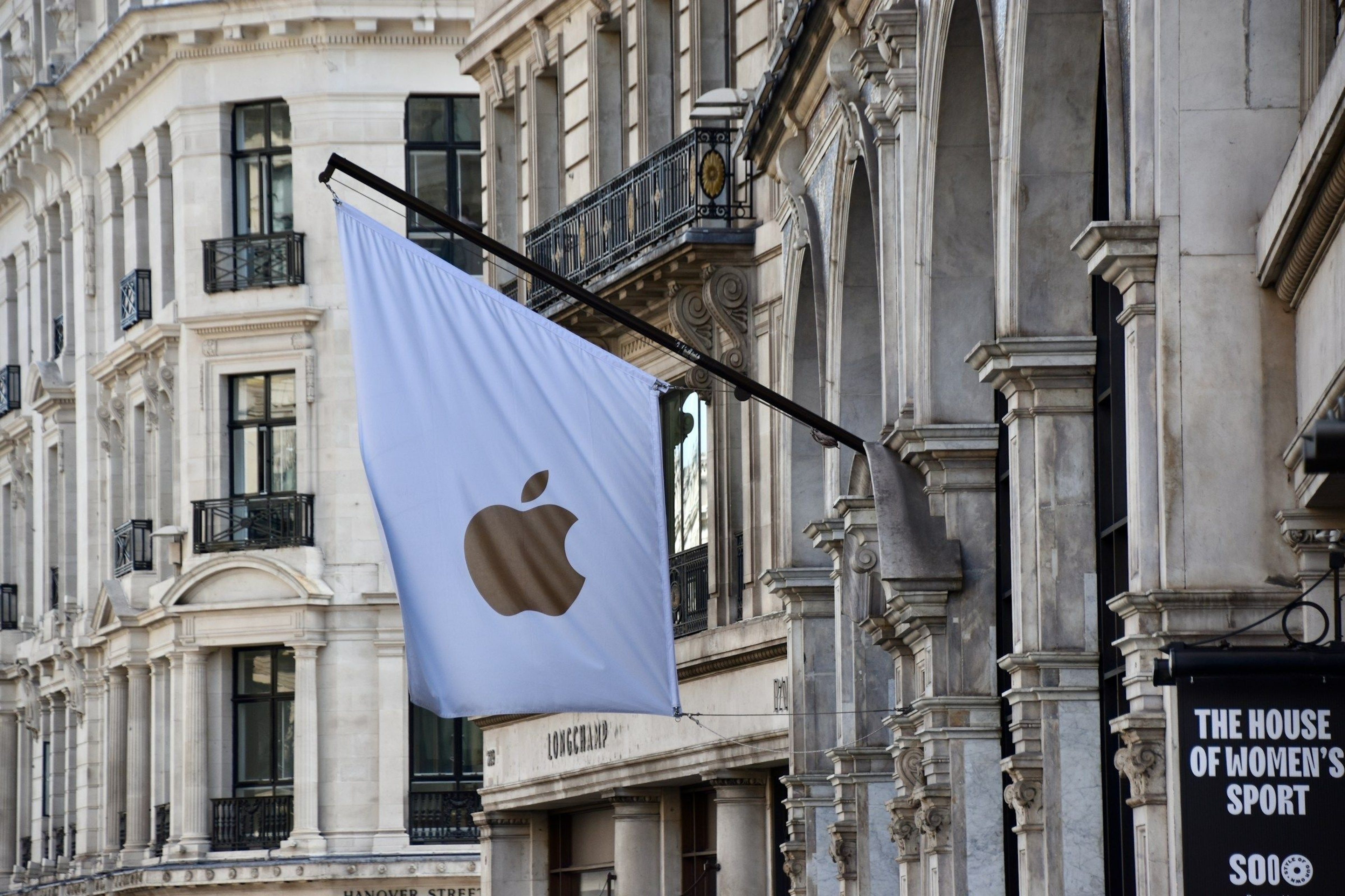 A white flag bearing the gold Apple logo hangs from an ornate classical building facade on a London shopping street