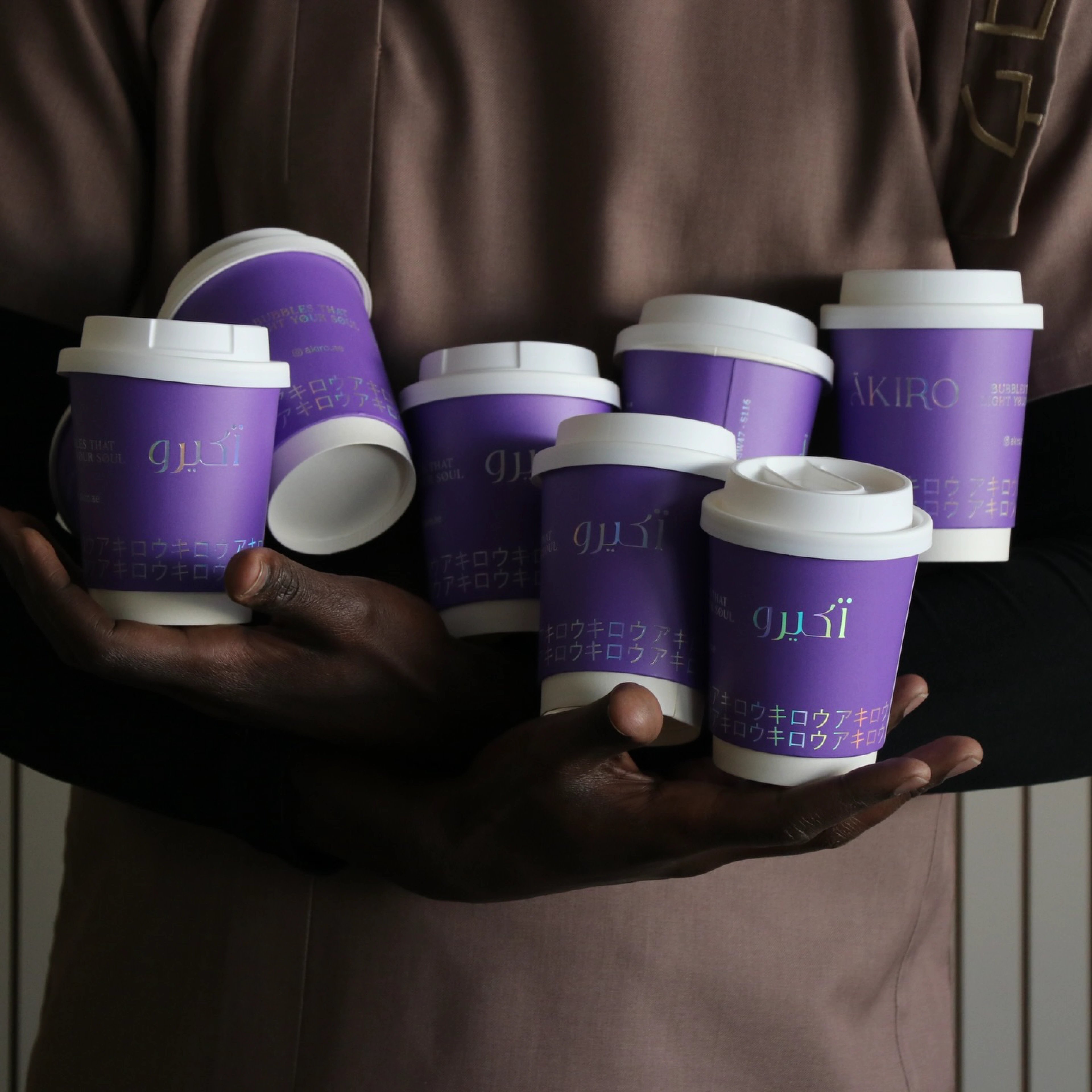 Hands holding a cluster of purple ÄKIRO branded coffee cups