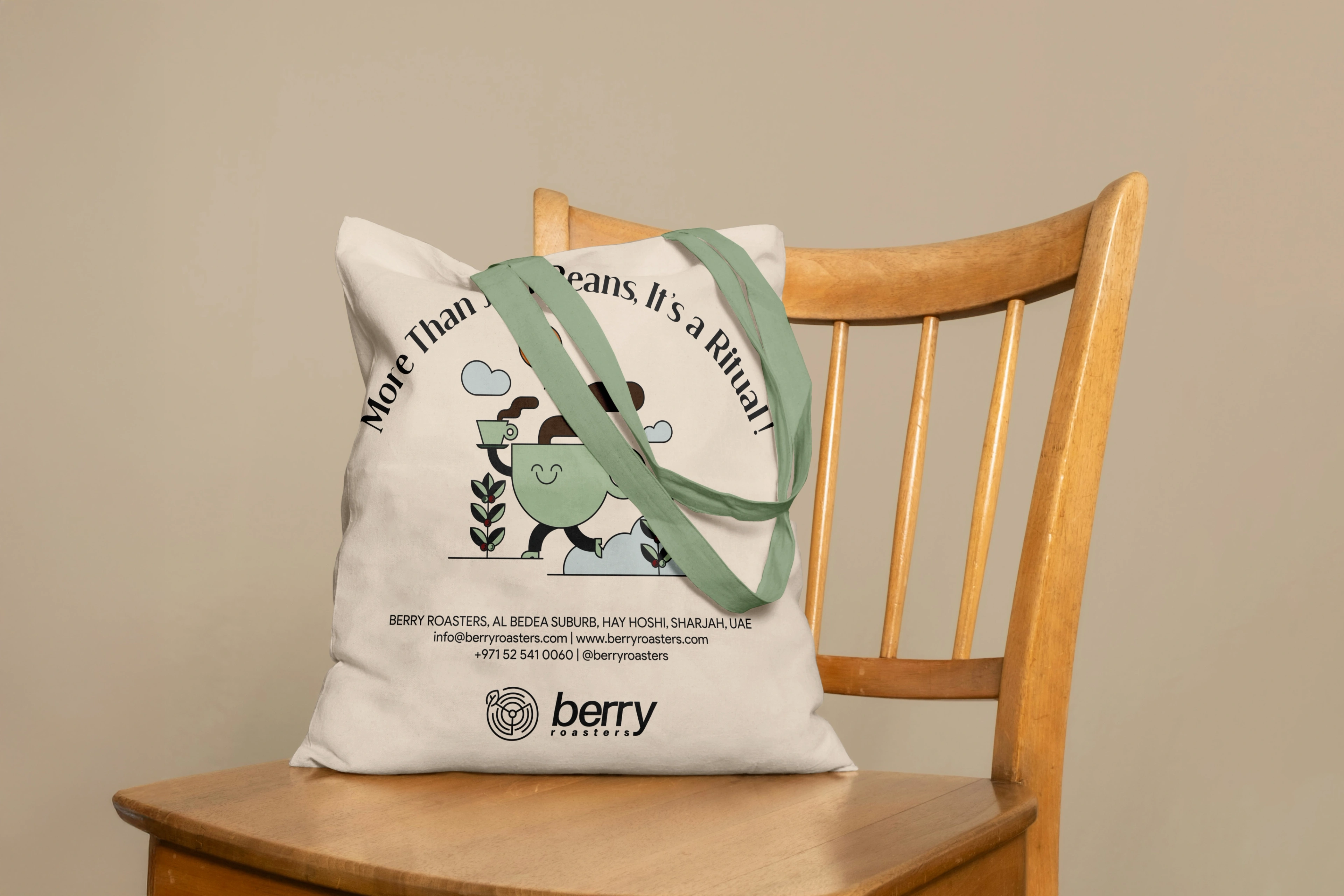 A Berry Roasters canvas tote bag resting on a wooden chair, printed with the 'More Than Just Beans, It's a Ritual' character illustration