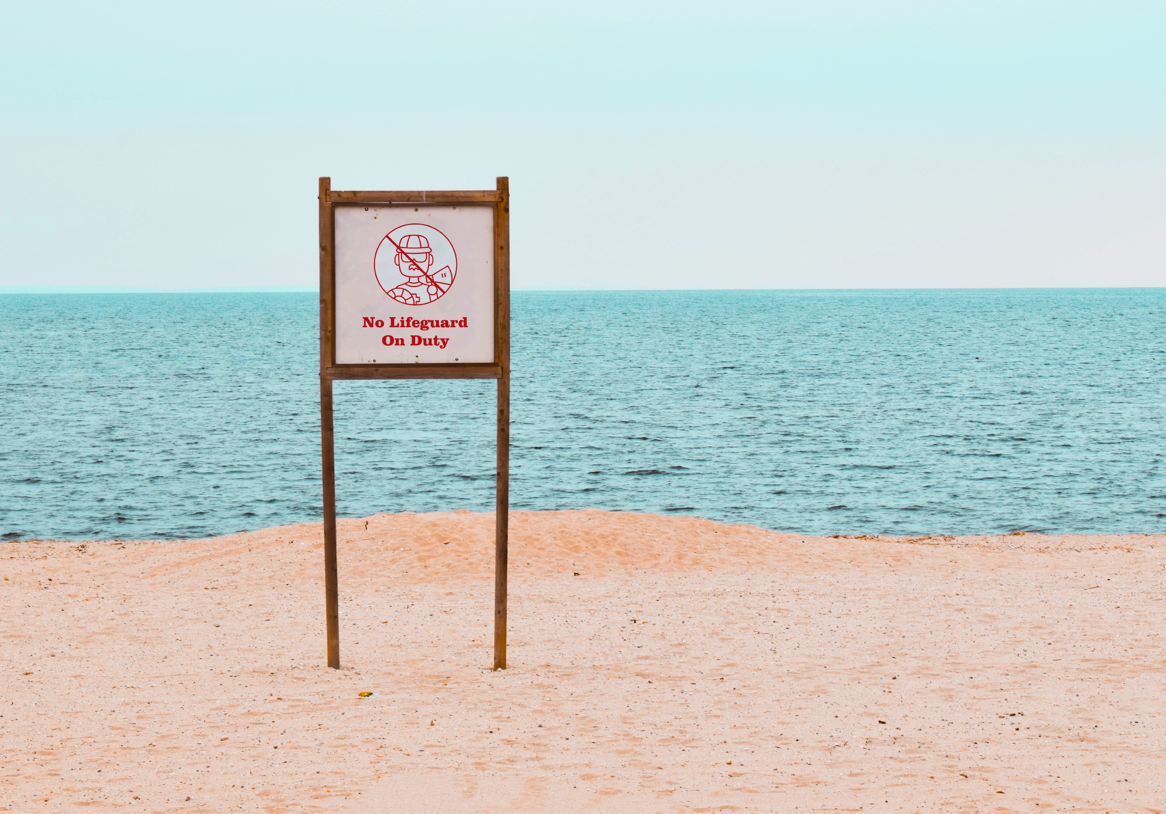 A 'No Lifeguard on Duty' Sawa Sawa beach sign staked in the sand at the ocean's edge