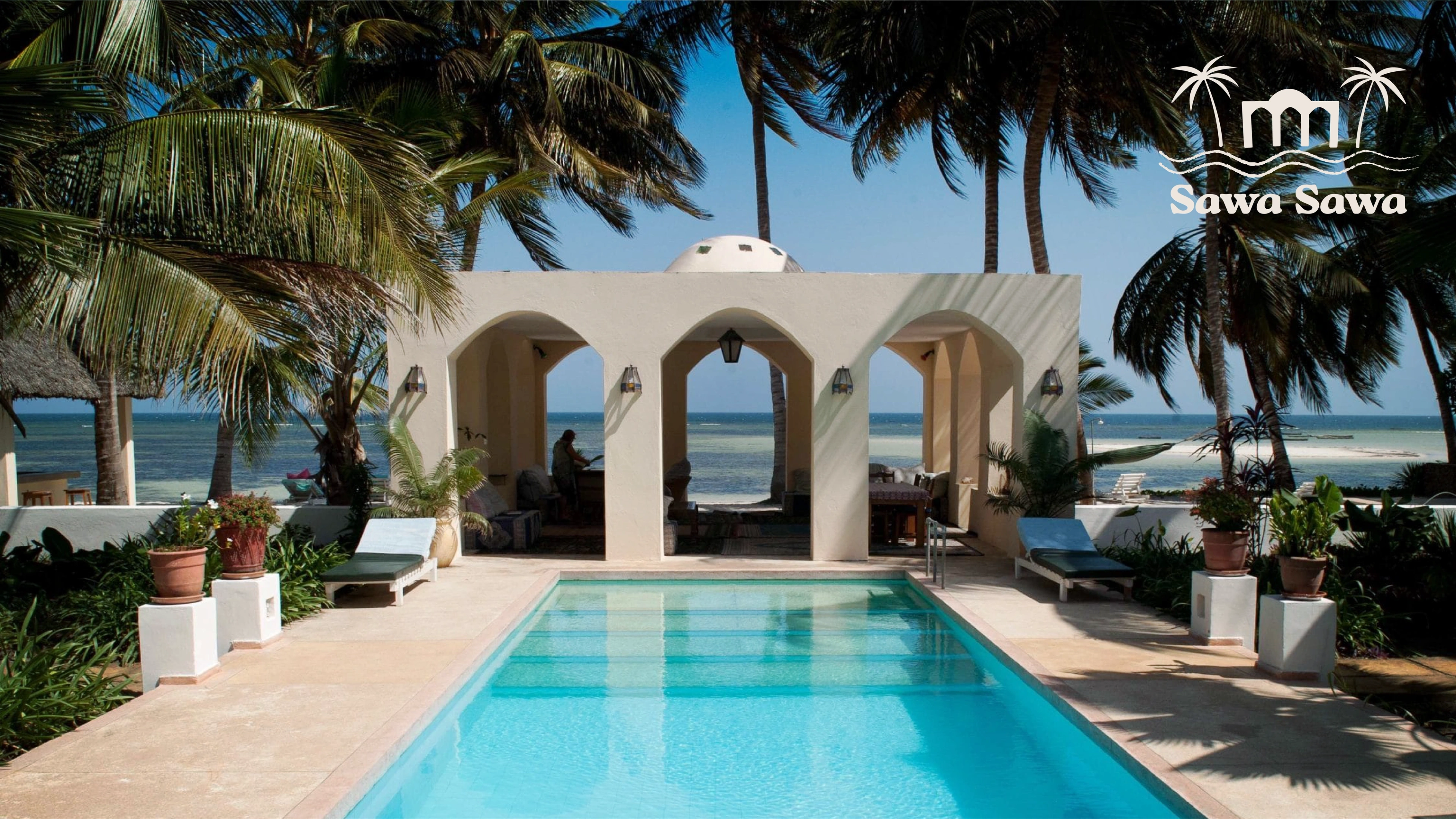 Sawa Sawa Beach House poolside framed by whitewashed arches, palms and the Indian Ocean beyond
