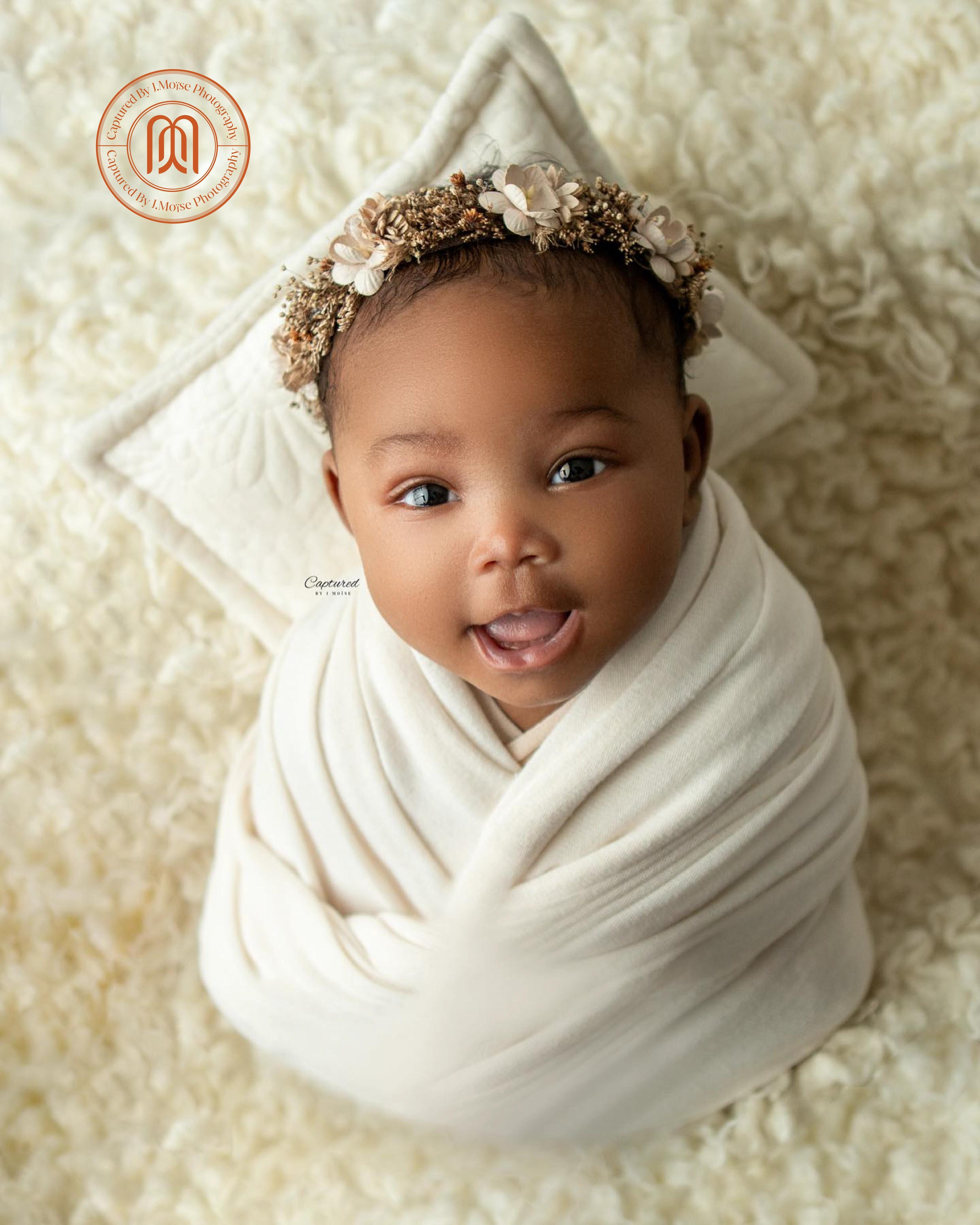 a newborn swaddled in cream lying on soft fur, the studio monogram in the corner