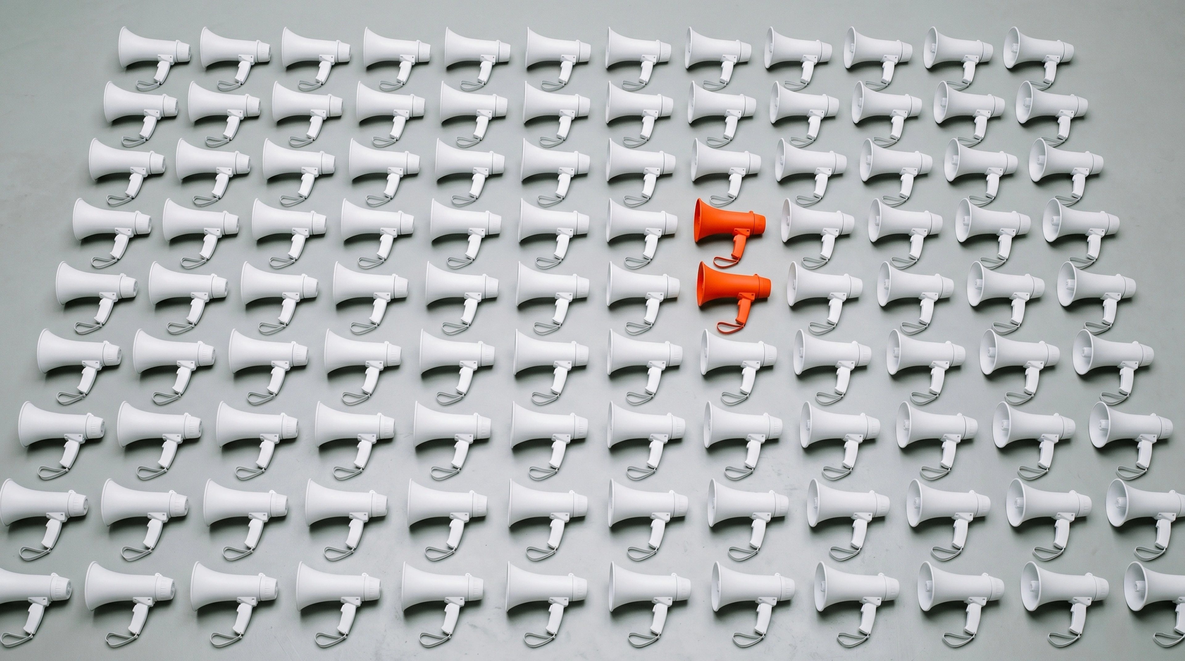 Grid of identical white megaphones with a single orange one standing out