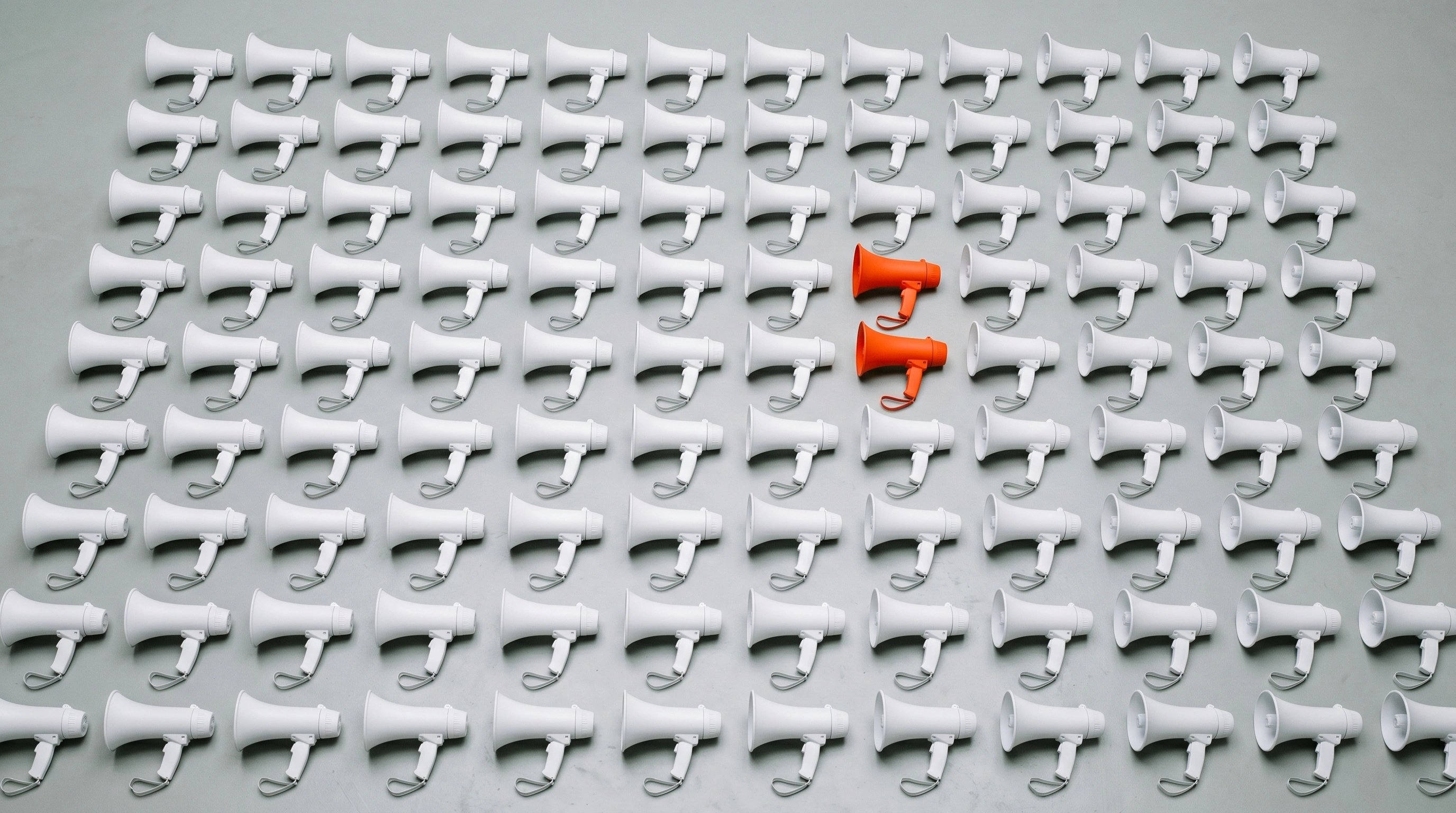 Grid of identical white megaphones with a single orange one standing out